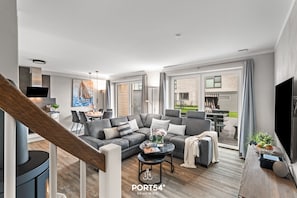 A modern living room with a grey sectional sofa, a coffee table, and a TV. There is a staircase with a wooden handrail leading to an upper floor.