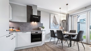 Una cocina moderna con armarios blancos, horno empotrado y comedor con mesa y sillas.