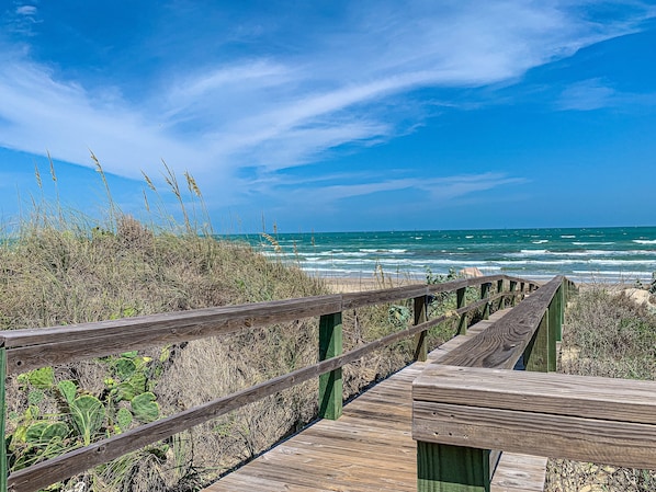 Une promenade en bois menant à une plage avec vue sur l’océan.