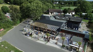 Ein Außenbereich mit Tischen und Stühlen, eine überdachte Terrasse und ein Gebäude mit Flachdach.