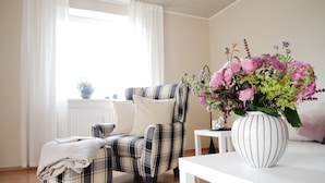 Ein Wohnzimmer mit einem karierten Sessel, einem weißen Beistelltisch mit Blumenvase und einem weißen Tisch.