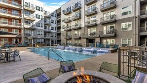 A multi-story residential building with balconies, a swimming pool, outdoor seating, and a fire pit. - Boulevard Stays Elegant 1BR Pool, Gym, Parking (Richardson)