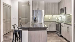 A modern kitchen with a central island, stainless steel appliances, and light wood cabinetry. - Boulevard Stays Elegant 1BR Pool, Gym, Parking (Richardson)