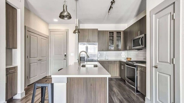A modern kitchen with a central island, stainless steel appliances, and wooden cabinetry. - Boulevard Stays Dashing 1BR Suite Pool, Parking Gym G (Richardson)