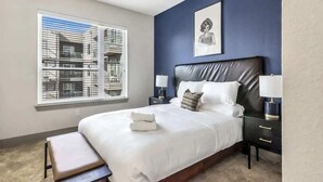 A bedroom with a bed, bedside tables, a bench, a window with blinds, and a ceiling fan. - Boulevard Stays Dashing 1BR Suite Pool, Parking Gym G (Richardson)