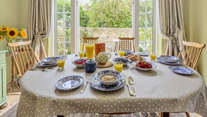 Una mesa de desayuno dispuesta con platos, tazones y cubiertos, con vistas a la vegetación.