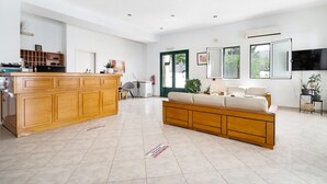 A spacious living area with a wooden sofa, a kitchen with wooden cabinets, and a large TV on the wall. - Apartment in a Hotel 'Sunset Premium Studio 5' with Sea View, Shared Pool, & Wi-Fi (Lefkada)