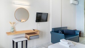 A modern hotel room with a flat-screen TV, a round mirror, a wooden desk with a drawer, a blue sofa, and a bed with a folded towel. - Apartment in a Hotel 'Sunset Premium Studio 5' with Sea View, Shared Pool, & Wi-Fi (Lefkada)
