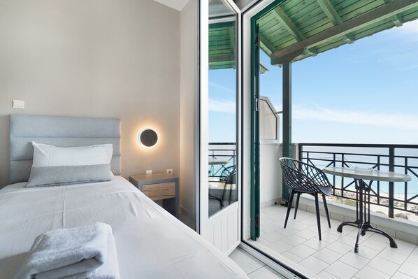 Une chambre d’hôtel moderne, équipée d’un lit, d’une petite table de chevet, d’une applique murale ronde et d’un balcon avec une table et des chaises.