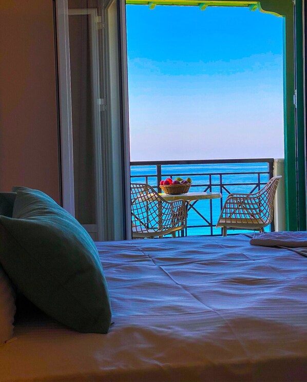 Habitación de hotel con cama, vista al mar y una mesa con sillas afuera.