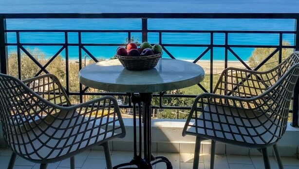 A balcony with a table and chairs, a basket of fruit, and a view of the sea. - Apartment in a Hotel 'Sunset Premium Studio 3' with Sea View, Shared Pool, & Wi-Fi (Lefkada)
