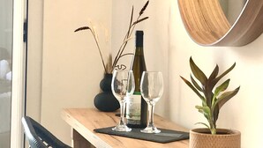 A wooden table with a wine bottle and two glasses, a potted plant, and a mirror on a wall. - Apartment in a Hotel 'Sunset Premium Studio 3' with Sea View, Shared Pool, & Wi-Fi (Lefkada)