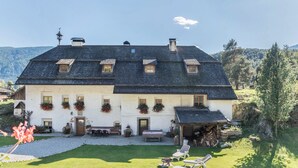 A white building with a dark roof, multiple windows, and a covered area with outdoor seating. - Oberwieserhof Apartment 3 in South Tyrol with Shared Garden and Wi-Fi (St.Lorenzen)