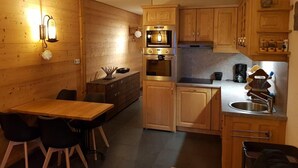 Una cocina compacta con armarios de madera, horno integrado, pileta y comedor con mesa y sillas.