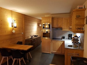 Eine kleine Küche mit Holzschränken, einem Einbauofen, einem Spülbecken und einem Essbereich mit Tisch und Stühlen.
