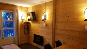 Interior acogedor de una cabaña con detalles de madera, chimenea, televisor montado en la pared y comedor con mesa y sillas.