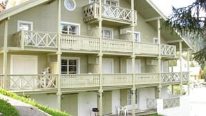 Un edificio de varios pisos con balcones, una terraza de madera y un pequeño jardín.