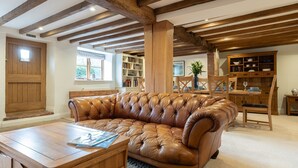 A cozy living room with a leather sofa, wooden coffee table, and exposed wooden beams on the ceiling. - Family friendly period holiday cottage in the Cotswolds - The Old Post Office (Ilmington, near Chipping Campden)