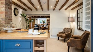 A cozy room with exposed wooden beams, a dining area with a table and chairs, and a blue cabinet with drawers. - Family friendly period holiday cottage in the Cotswolds - The Old Post Office (Ilmington, near Chipping Campden)