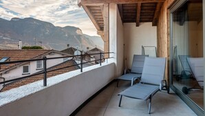 Un balcón con vista a las montañas, un ventanal de vidrio y dos sillones de descanso.