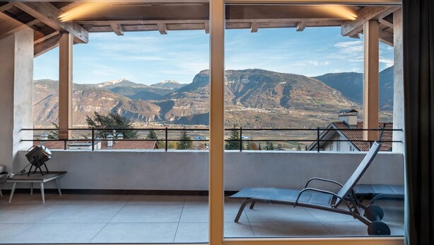 Un balcón con vistas a las montañas, una mesa con una silla y una tumbona.