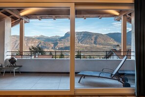 Un balcon avec vue sur les montagnes, une table avec une chaise et un transat.
