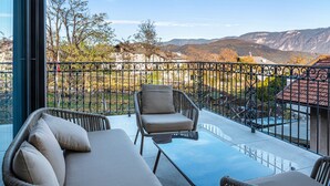 Un balcón con mobiliario de mimbre, una mesa de vidrio y vistas a montañas.