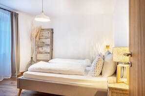 Un lit bien fait, avec une literie blanche, une tête de lit en bois et une table de chevet surmontée d’une lampe.