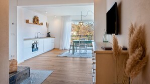Una cocina moderna con armarios blancos, una mesa de comedor de madera y un televisor montado en la pared.