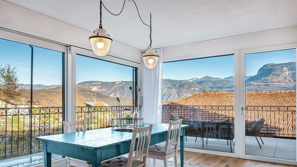 Un comedor con una mesa y sillas, amplias ventanas con vistas a la montaña y lámparas colgantes.
