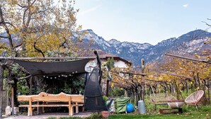 Ein rustikaler Sitzbereich im Freien mit einer Holzbank, einer Hängematte und einem Stuhl, vor einer Kulisse aus Bergen und Herbstlaub.