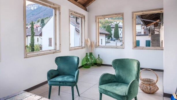 Ein Zimmer mit Holzboden, großen Fenstern, zwei grünen Stühlen und einem Korbwäschekorb.