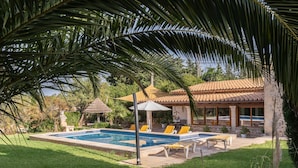 A pool area with lounge chairs, a pergola, and a stone building with a tiled roof. - Villa Can Tomas with Mountain View, Garden, Pool & Wi-Fi (Pollença)