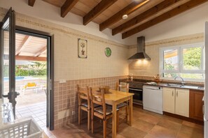 Una cocina con sillas de madera, una mesa de comedor, una estufa, un lavavajillas y un ventanal con vistas a la vegetación.