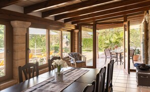 Un comedor con una mesa dispuesta para cuatro personas, rodeada de sillas, que ofrece vistas al jardín y al área de estar exterior.