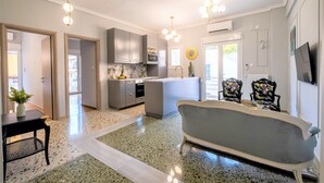 A modern kitchen with grey cabinets, a built-in oven, and a central island. There is a dining area with a vintage-style sofa and two patterned chairs. - Luxury Penthouse in prime central Athens Thissio (Athina)