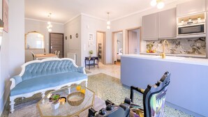 A modern living room with a blue sofa, a coffee table, and a chair. There is a kitchen area with a marble countertop and a sink. - Luxury Penthouse in prime central Athens Thissio (Athina)