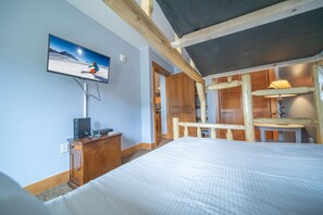 Ein Hotelzimmer mit einem Bett, einem Fernseher der eine Skiszene zeigt, einem Holztisch und einer Lampe.