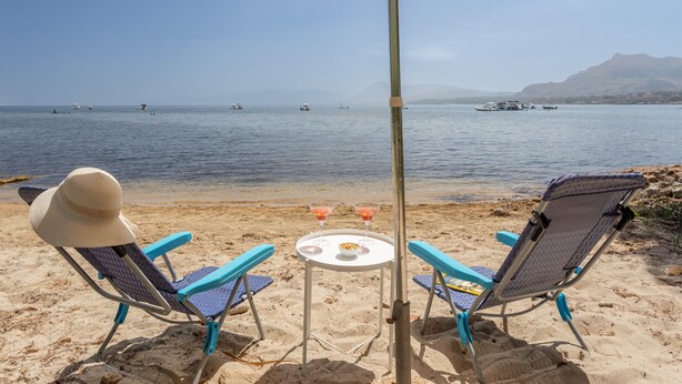 Una playa con dos sillas y una mesa bajo un paraguas a rayas, con vista al mar.