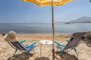 Una playa con dos sillas y una mesa bajo un paraguas a rayas, con vista al mar.