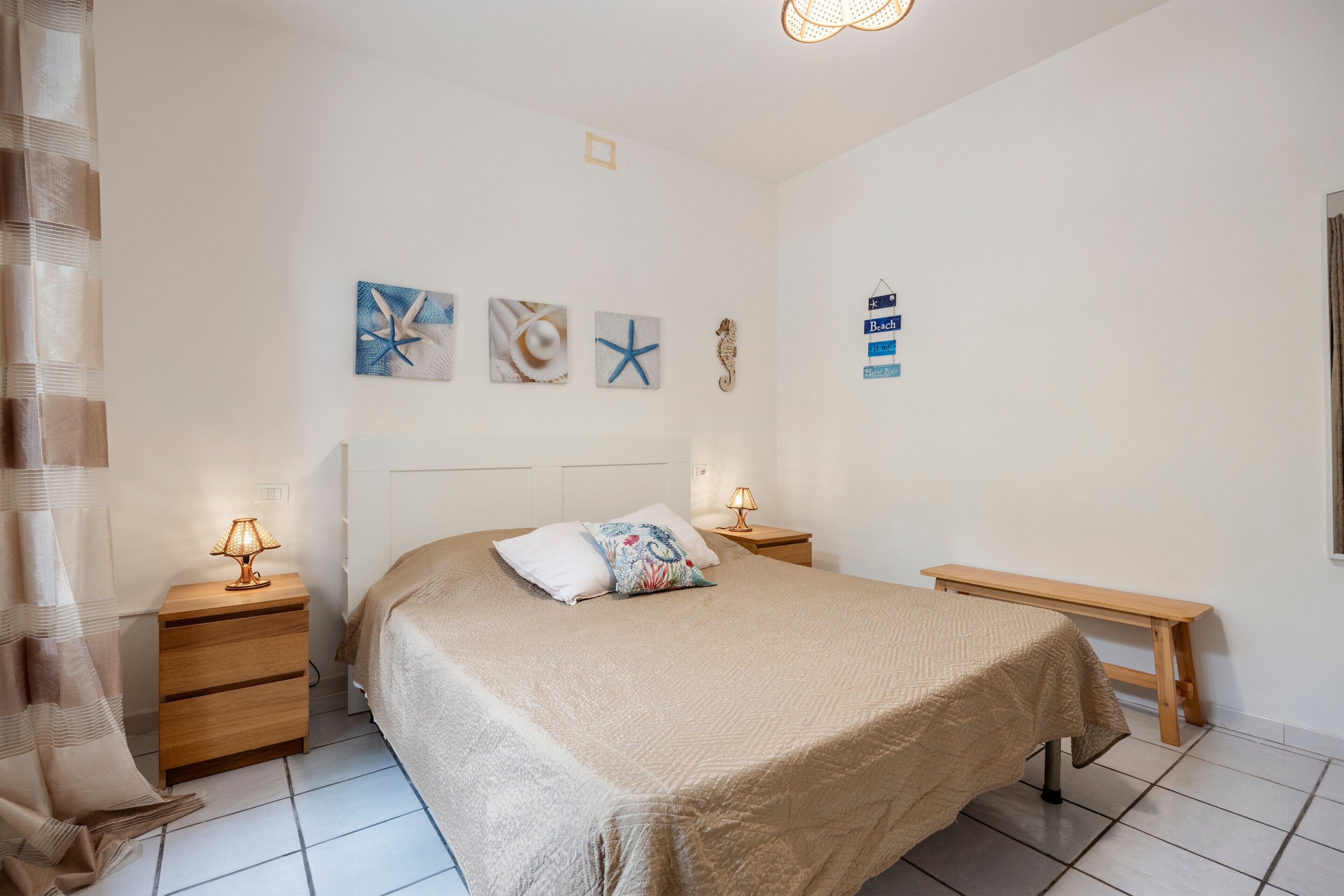 Une chambre à coucher comprenant un lit, des tables de chevet, un banc et des œuvres d’art murales.