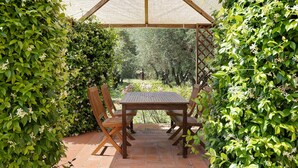 A covered patio with a wooden table and chairs, surrounded by lush greenery. - 'La Ripa - Apartment Il Fienile' with Shared Pool & Wi-Fi (San Gimignano)