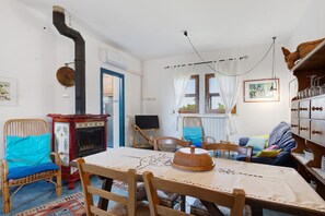 A room with a wooden table, chairs, a fireplace, a television, and a window with curtains.