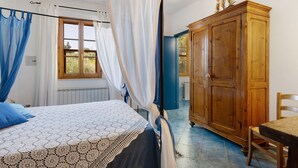 A bedroom with a bed, a wooden wardrobe, a table, and a window with curtains. - 'La Ripa - Apartment Il Fienile' with Shared Pool & Wi-Fi (San Gimignano)