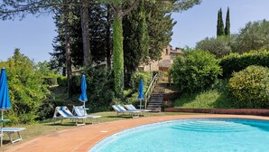 A swimming pool with lounge chairs and umbrellas, surrounded by greenery and a stone building. - 'La Ripa - Apartment Il Fienile' with Shared Pool & Wi-Fi (San Gimignano)