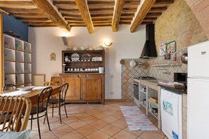 Una cocina con mesa de madera, sillas, un armario, lavavajillas y salpicadero de azulejos.