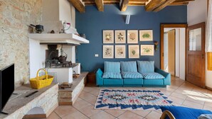 A cozy living room with a stone wall, wooden beams, a blue sofa, a patterned rug, and a fireplace. - 'La Ripa - Apartment I Ghiri' with Shared Pool & Wi-Fi (San Gimignano)