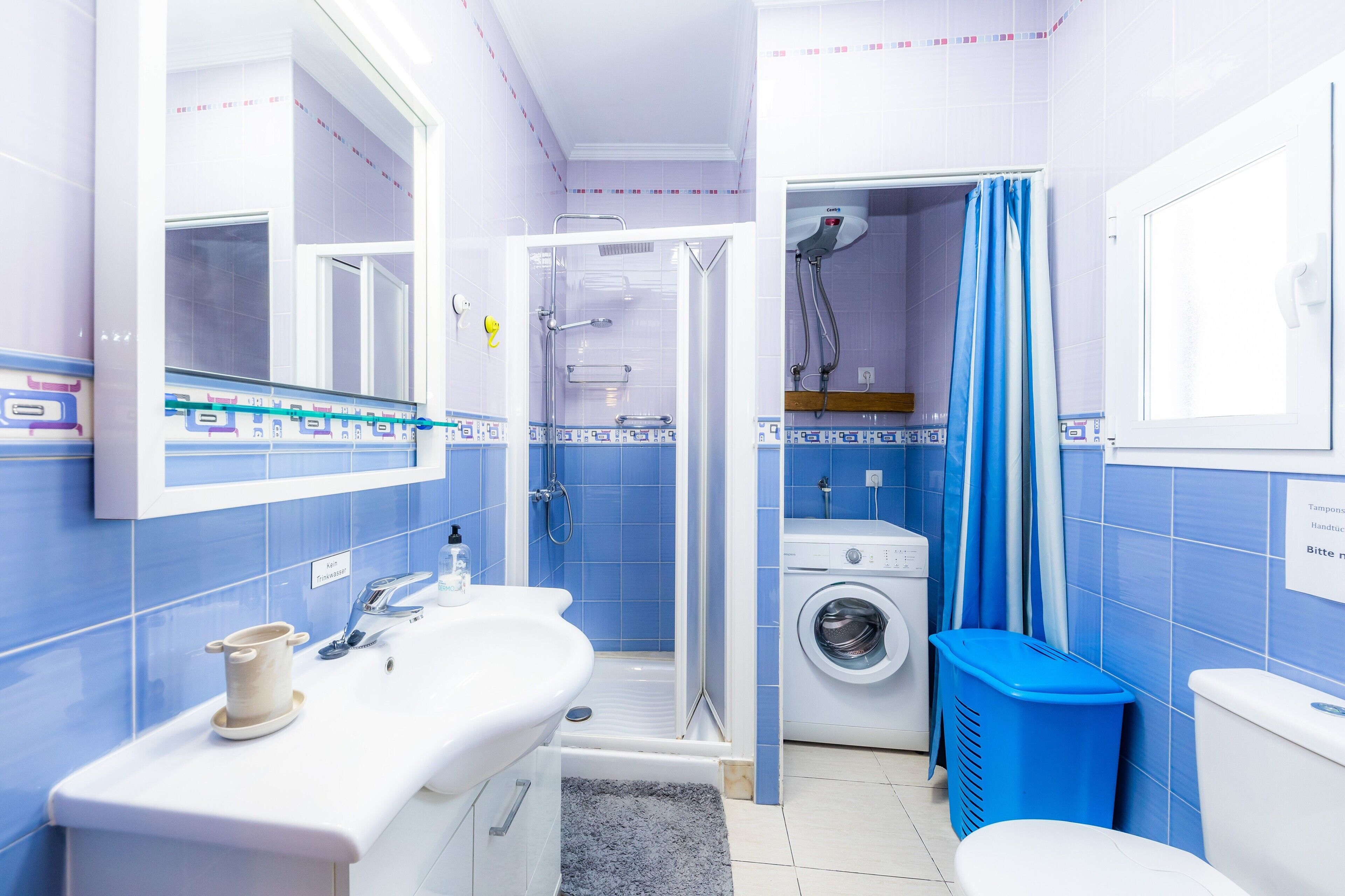 Ein Badezimmer mit Waschbecken, Spiegel, Dusche und Waschmaschine.