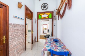 Un couloir étroit avec un mur en briques, des portes en bois, un coin repas avec une nappe à motifs et, au fond, une cuisine.