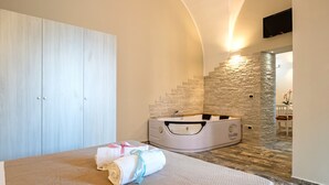 A bedroom with a large bed, a stone wall, a stone staircase, and a bathtub.